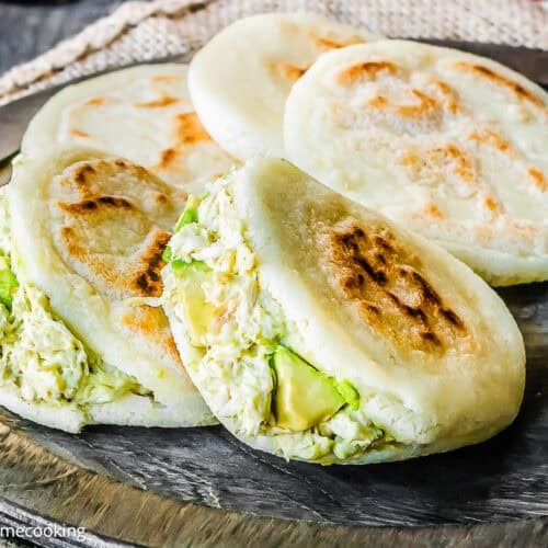 Three grilled arepas are filled with shredded chicken and avocado, resting on a wooden serving board—just like in classic How to Make Venezuelan Arepas (Arepas Venezolanas) recipes.