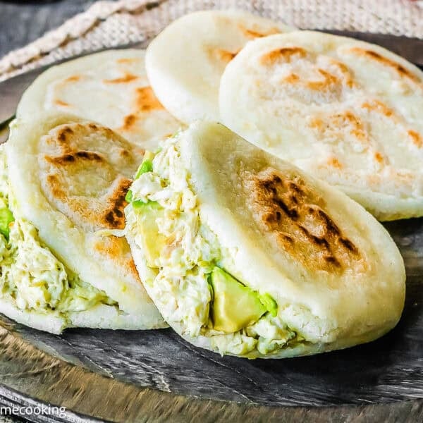 Three grilled arepas are filled with shredded chicken and avocado, resting on a wooden serving board—just like in classic How to Make Venezuelan Arepas (Arepas Venezolanas) recipes.