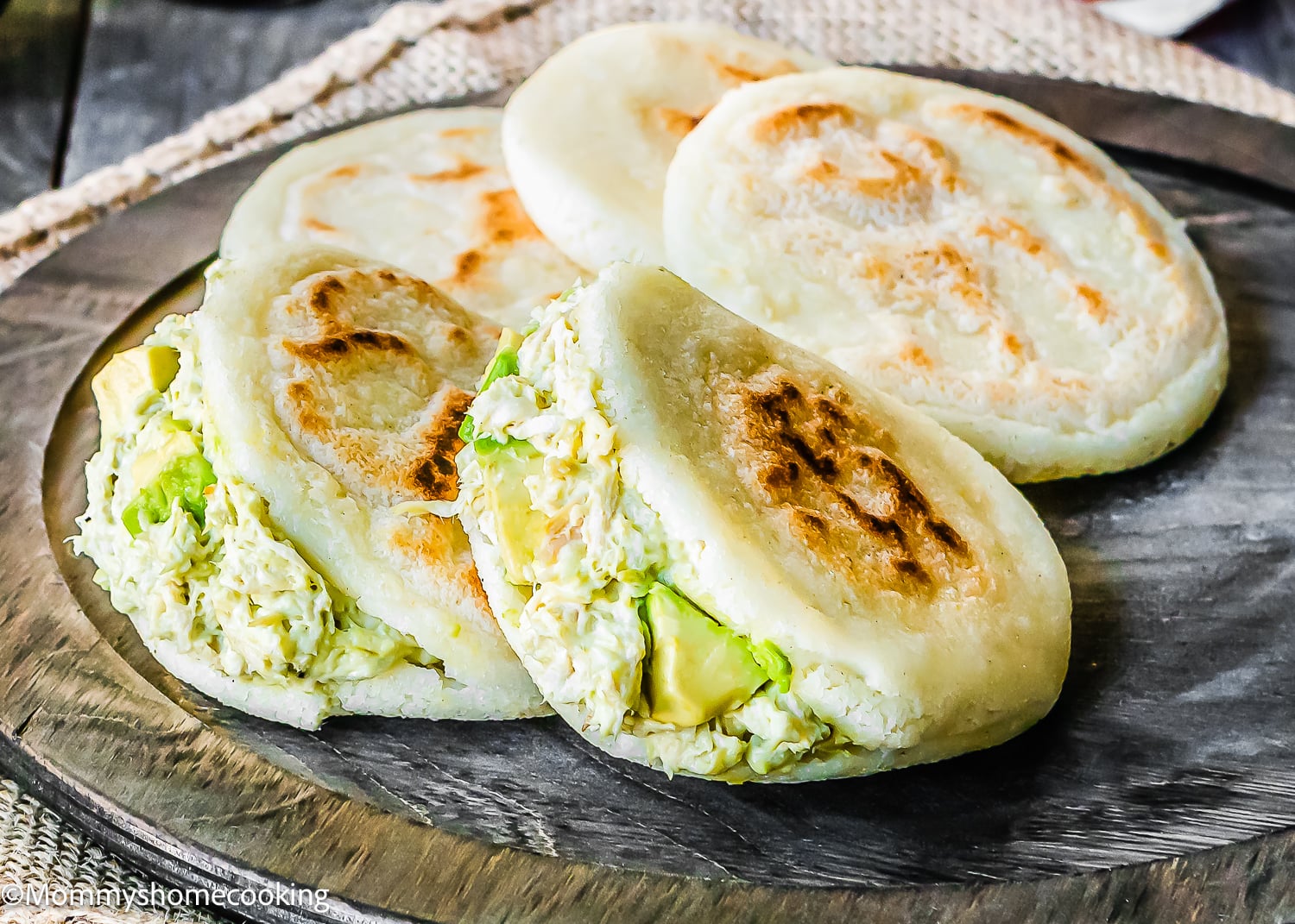Three grilled arepas are filled with shredded chicken and avocado, resting on a wooden serving board—just like in classic How to Make Venezuelan Arepas (Arepas Venezolanas) recipes.