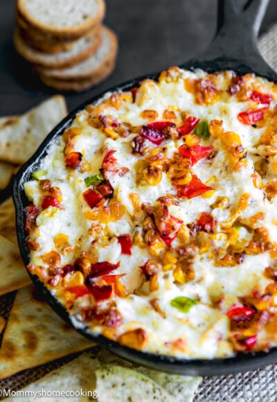 baked crab dip with roasted veggies in a cast iron skillet with cracker and chips on the side.