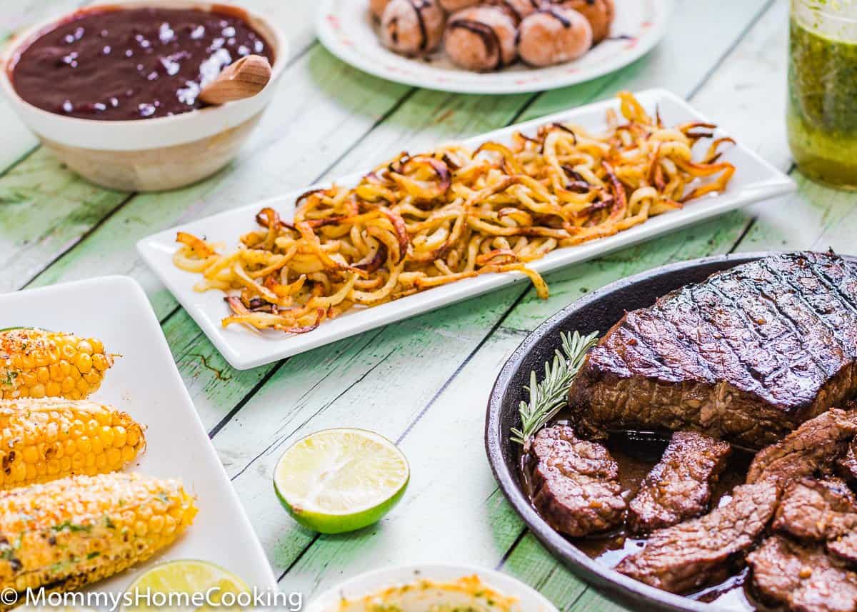 GRILLED BALSAMIC-GARLIC STEAK, curly fries, bbq sauce and corn on a green wooden table