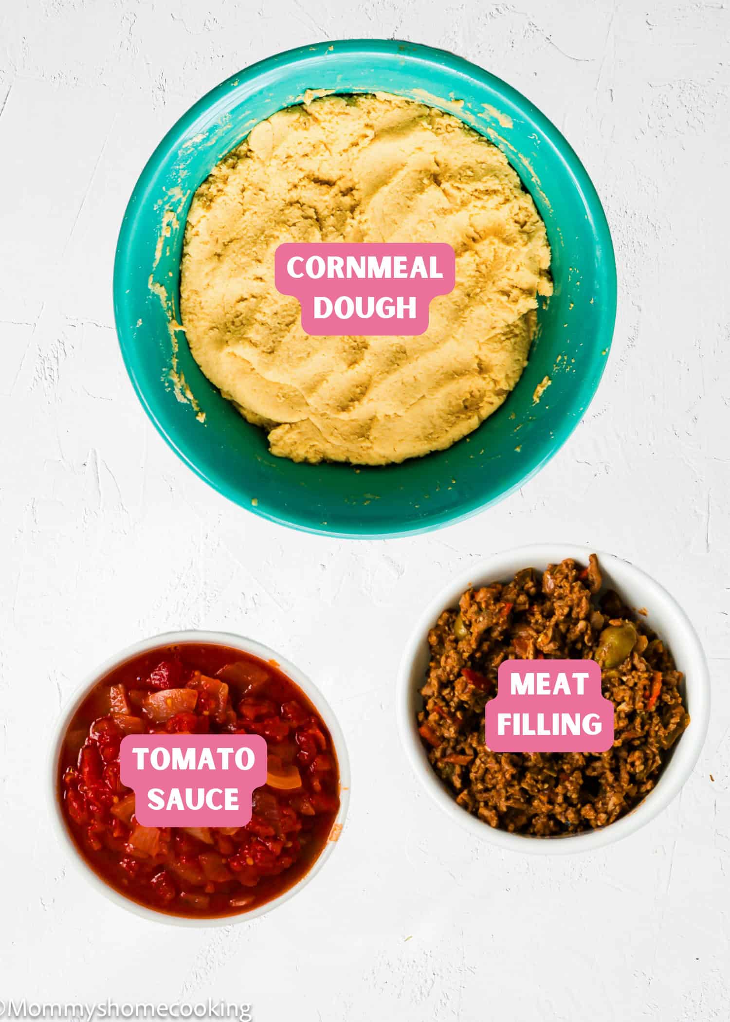 A bowl of cornmeal dough, a bowl of meat filling, and a bowl of tomato sauce—classic components for Venezuelan Bollos Pelones—are arranged on a white surface, each labeled accordingly.