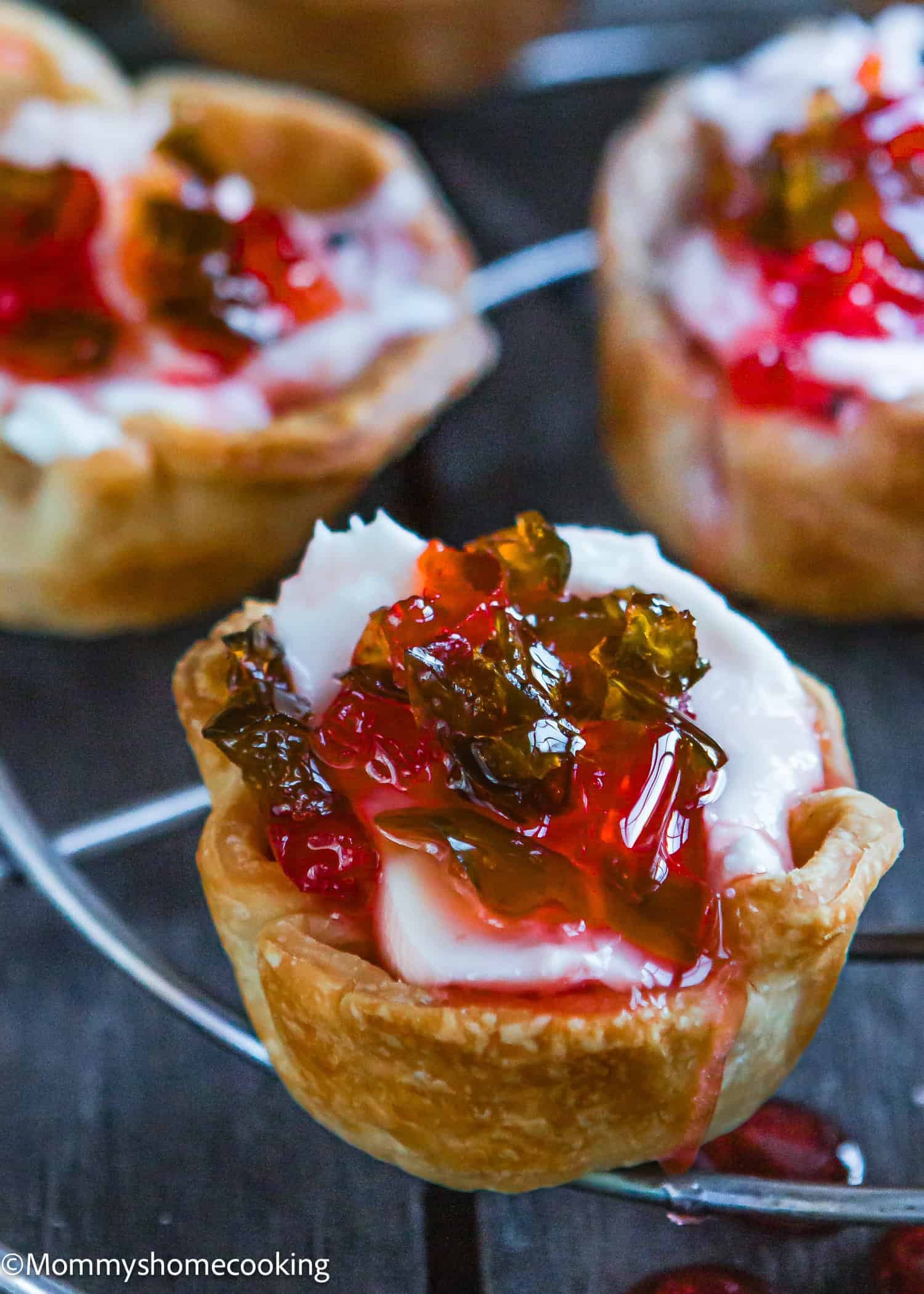 Close-up of a mini tart with a flaky crust, filled with creamy white Hot Pepper Jelly Cream Cheese and topped with vibrant red and green jelly for a sweet & spicy appetizer twist.