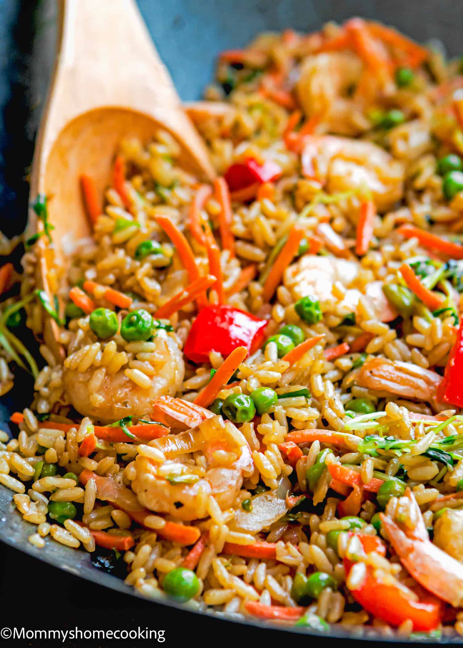 A pan of easy shrimp fried rice brimming with peas, carrots, and red bell peppers beckons, accompanied by a wooden spoon.