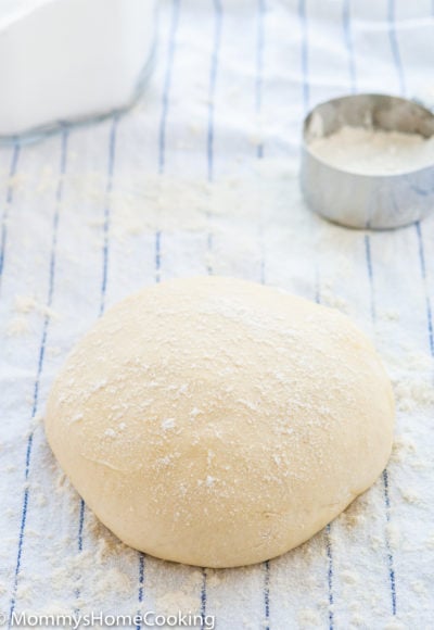 homemade pizza dough over a blue KITCHEN towel sprinkled with flour.
