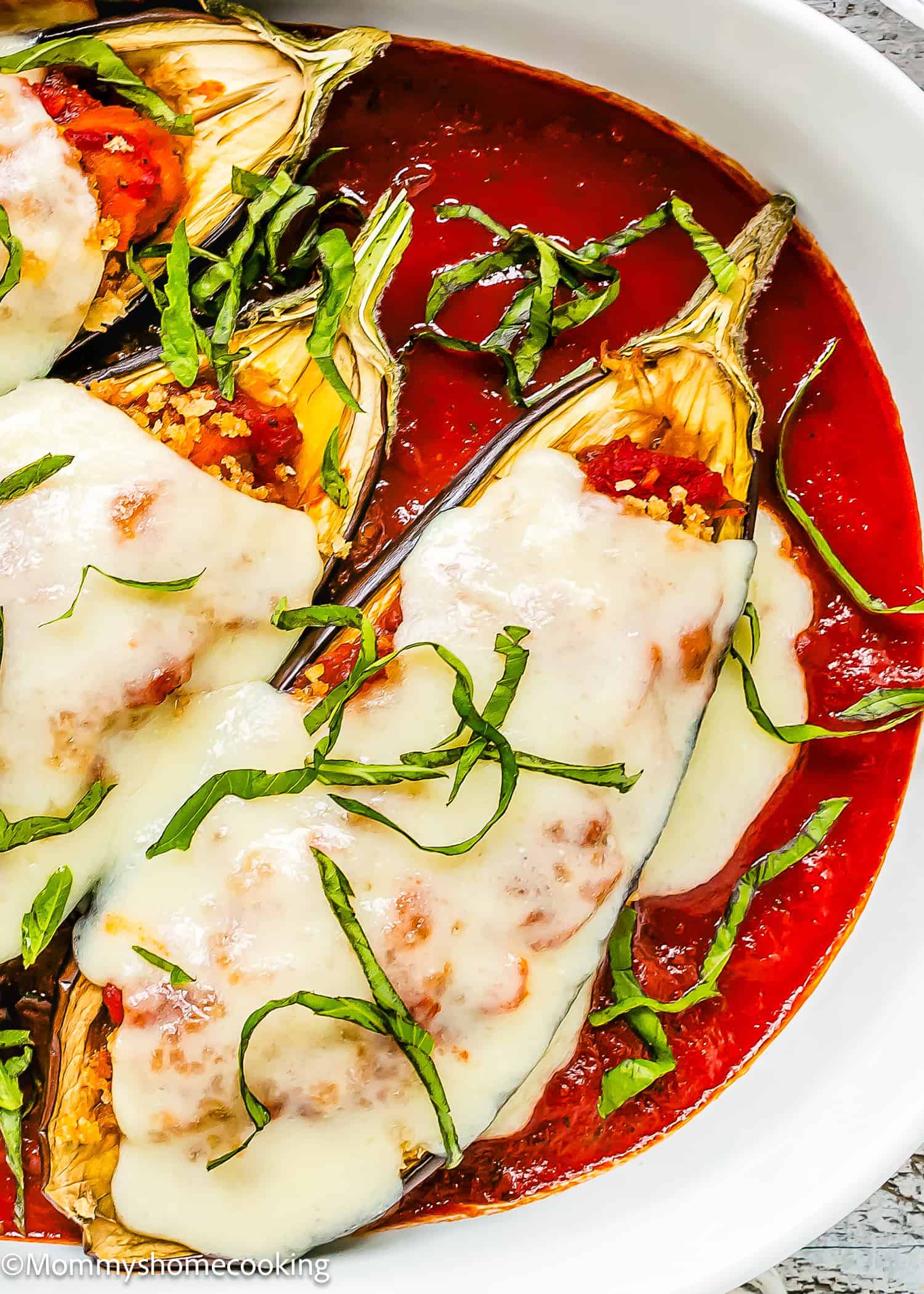 Stuffed Eggplant Parmesan Boats: Eggplant halves stuffed with a savory filling, topped with melted cheese and tomato sauce, then garnished with sliced fresh basil in a white dish.