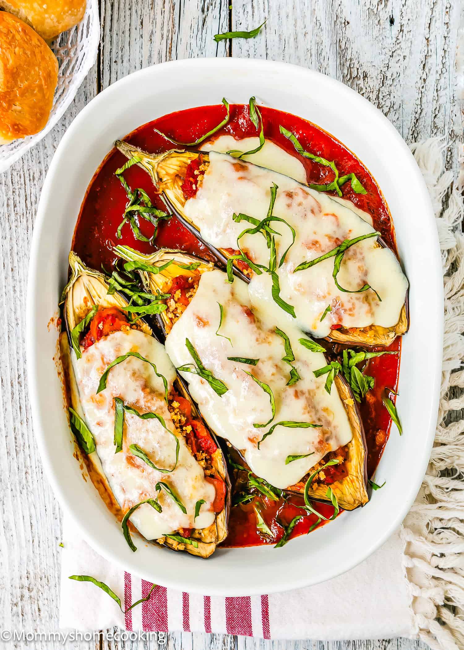 Stuffed Eggplant Parmesan Boats feature baked eggplant halves filled with savory stuffing, topped with melted cheese and fresh basil, all served in tomato sauce in a white oval dish.