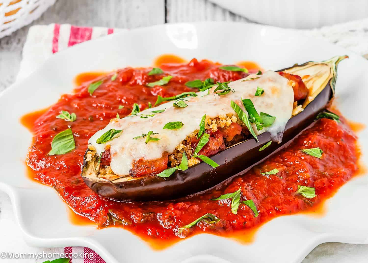 A halved eggplant transforms into Stuffed Eggplant Parmesan Boats, filled with a savory mixture, topped with melted cheese and herbs, and served on a bed of tomato sauce on a white plate.