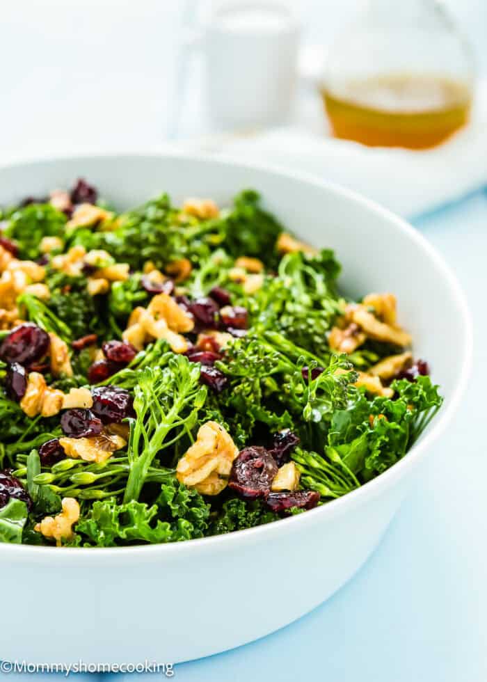 A white bowl containing a Chick-fil-A-inspired kale salad with walnuts, cranberries, and broccoli. Dressing is visible in the background.