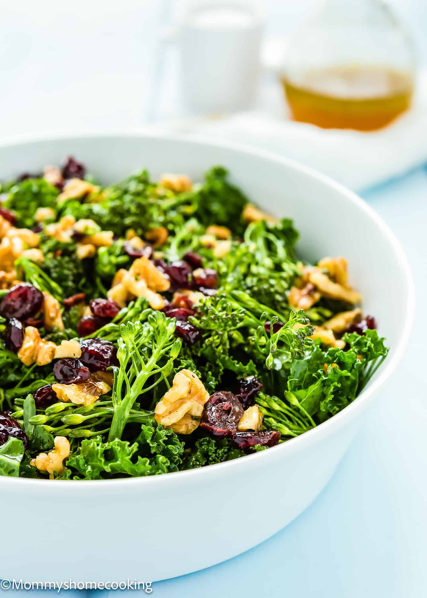A white bowl containing a Chick-fil-A-inspired kale salad with walnuts, cranberries, and broccoli. Dressing is visible in the background.