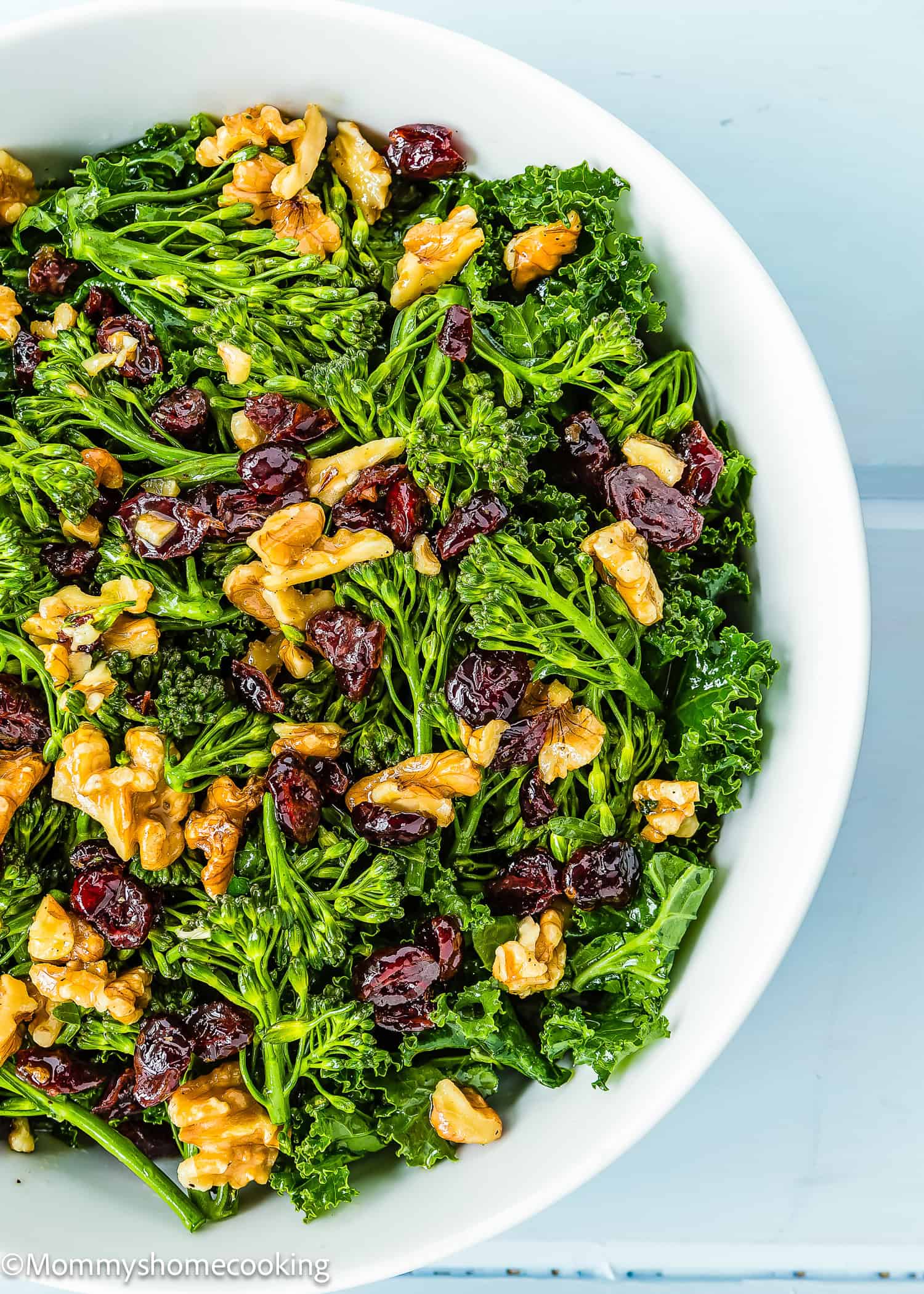 A bowl of Chick-fil-A kale salad with walnuts and cranberries rests on a light blue surface.