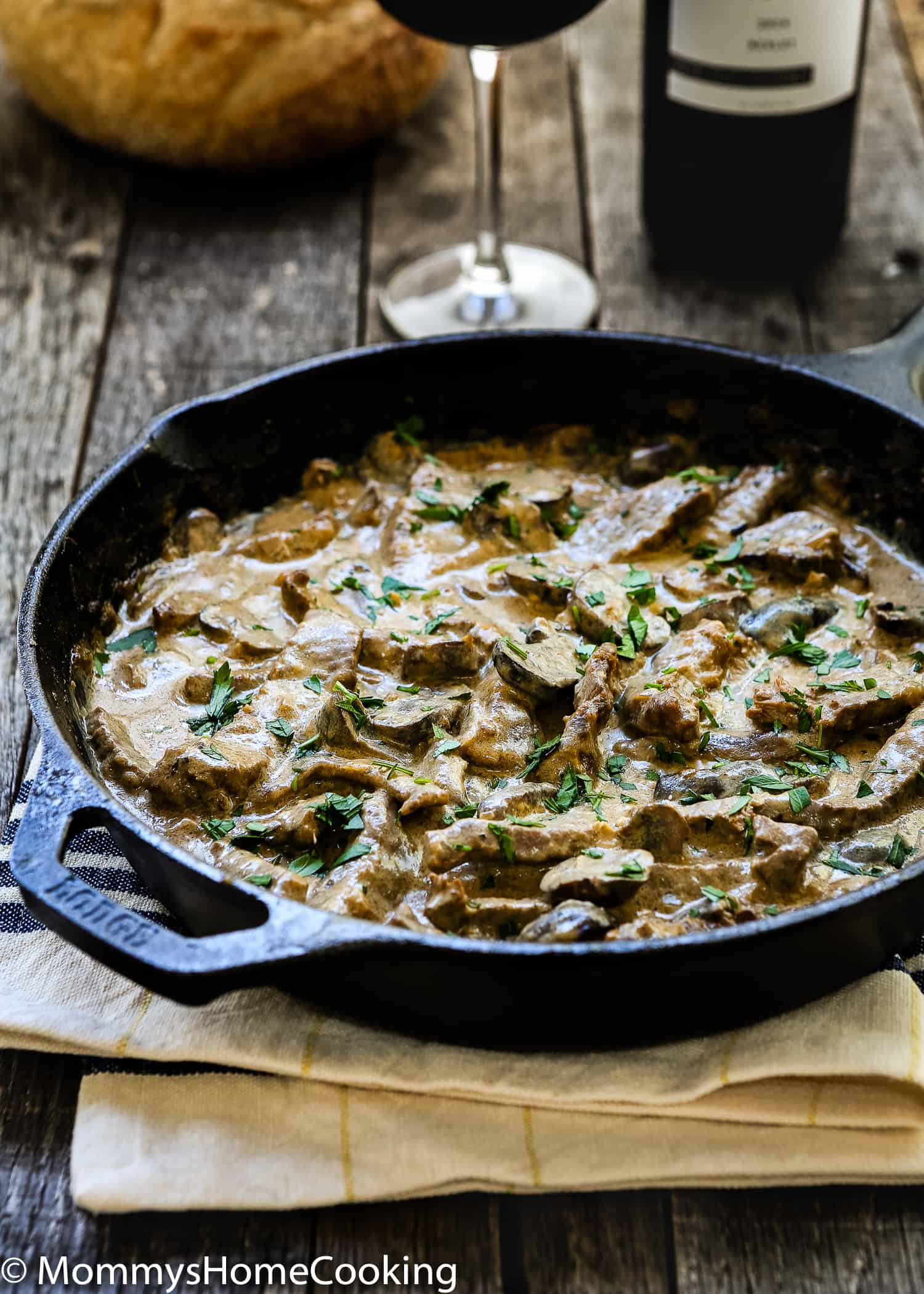 Beef Stroganoff in a skillet with a glass and bottle of wine in the background. 