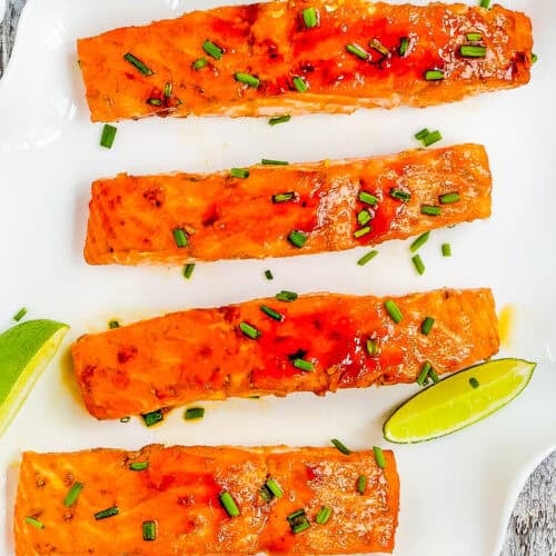 Easy Glazed Salmon fillets garnished with chopped chives are arranged on a white plate with lime wedges.