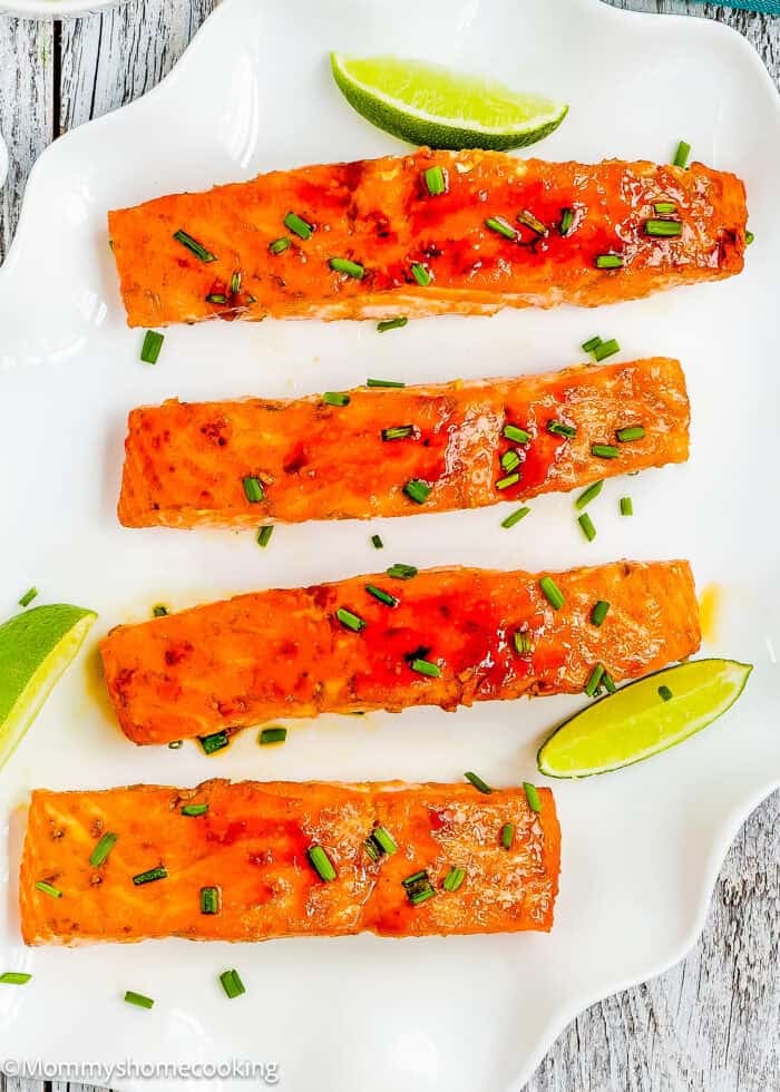 Easy Glazed Salmon fillets garnished with chopped chives are arranged on a white plate with lime wedges.