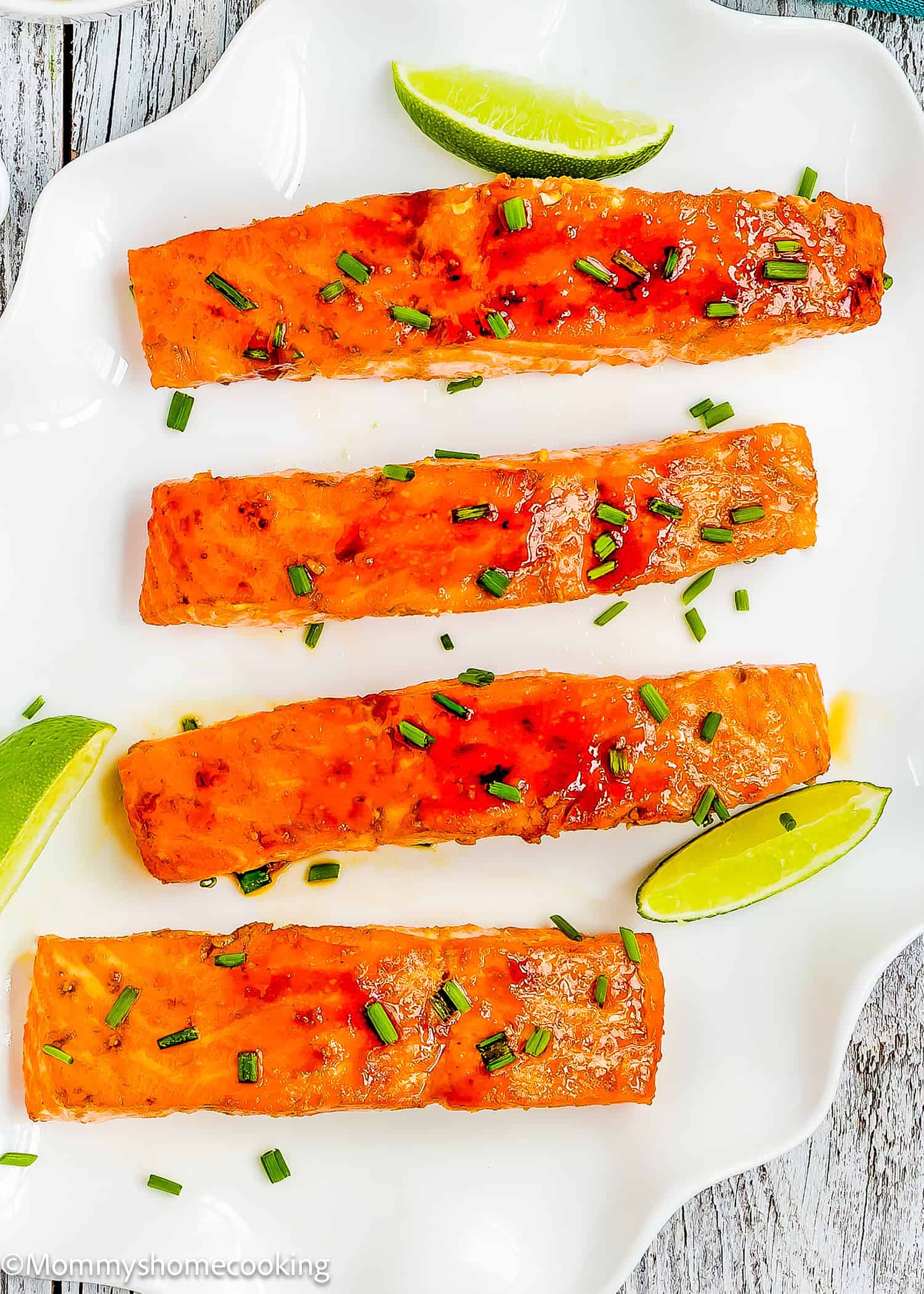 Easy Glazed Salmon fillets garnished with chopped chives are arranged on a white plate with lime wedges.
