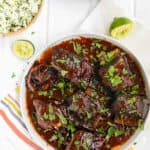 overhead view of mexican short ribs with sauce in a serving plate with chopped cilantro