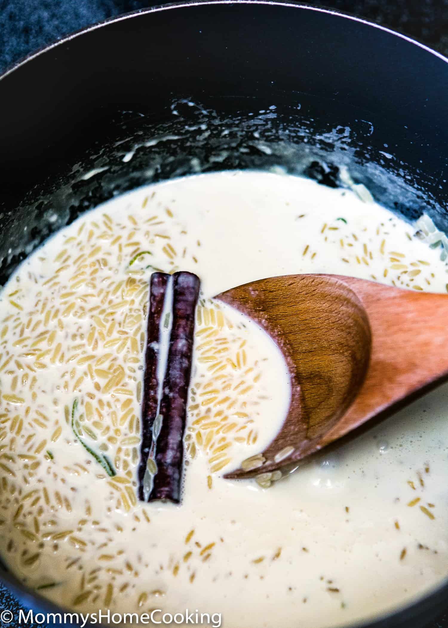 a pot with arroz, milk and a stick of cinnamon with a wooden spoon. 