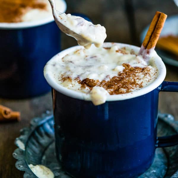 a spoon scooping arroz con leche from a blue cup over a metal plate.