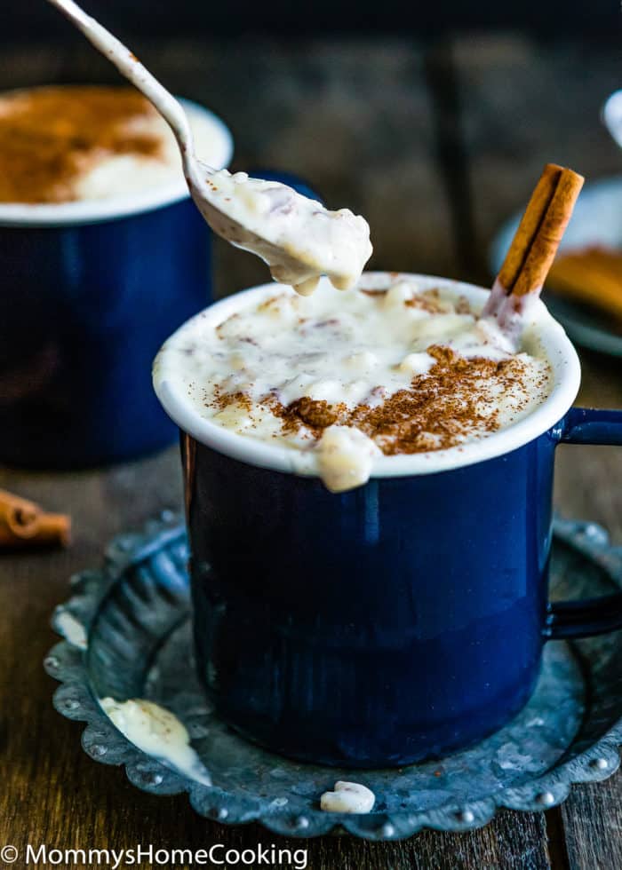 a spoon scooping arroz con leche from a blue cup over a metal plate.