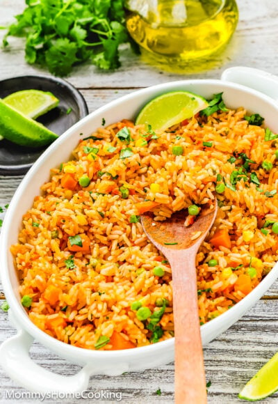 Easy Mexican rice in a serving bowl with lime wedges and a wooden spoon.