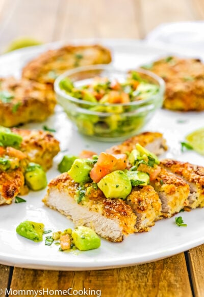 Healthy oven fried pork chops over a serving plate with avocado salad.