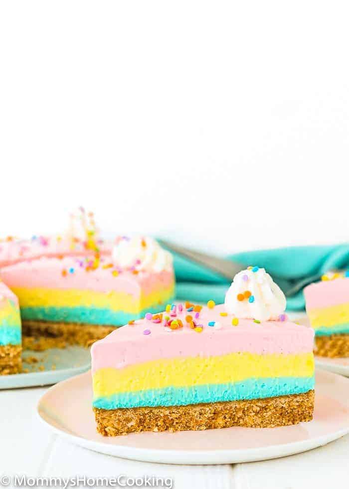 A slice of eggless no-bake cheesecake, layered in blue, yellow, and pink.