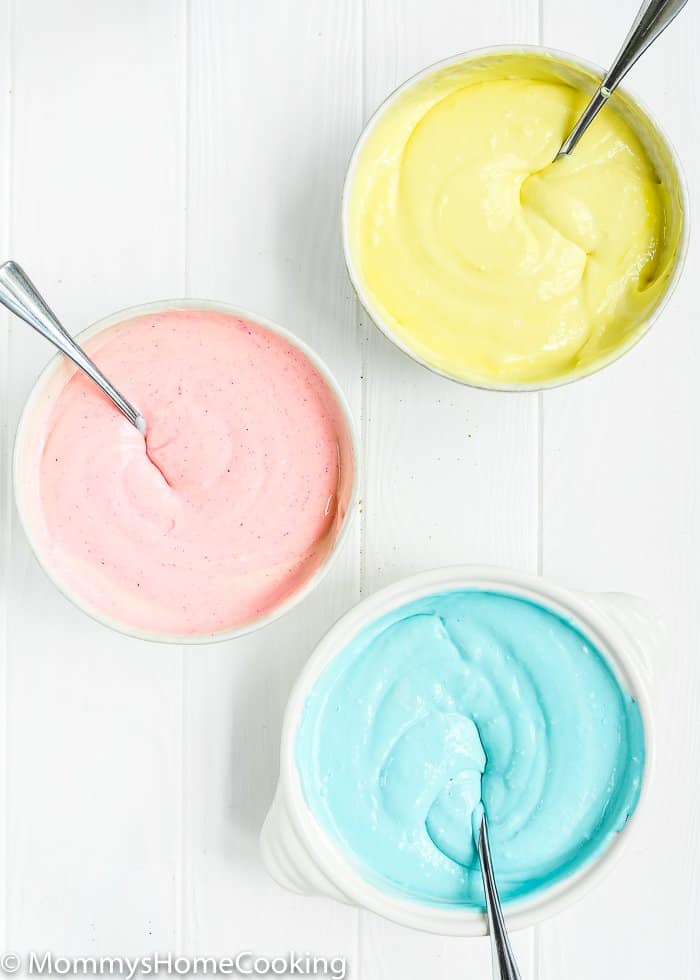 Cheesecake batter in three bowls colored in different colours: yellow, pink, and blue.