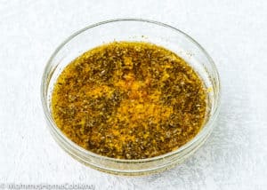 A clear glass bowl filled with a mixture of oil and dried herbs, perfect for marinating Instant Pot Mojo Chicken, sits on a light textured surface.