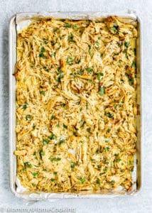 A baking sheet filled with seasoned, shredded Instant Pot Mojo Chicken garnished with chopped herbs on a parchment-lined surface.