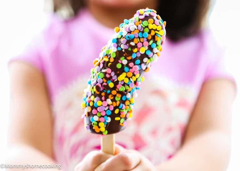 A child holds one of these Easy Frozen Banana Pops: a chocolate-covered banana on a stick, coated with colorful sprinkles.