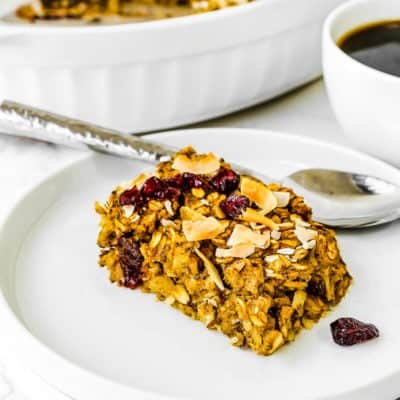a portion of Eggless Pumpkin Baked Oatmeal on a plate with a cup of coffee on the background