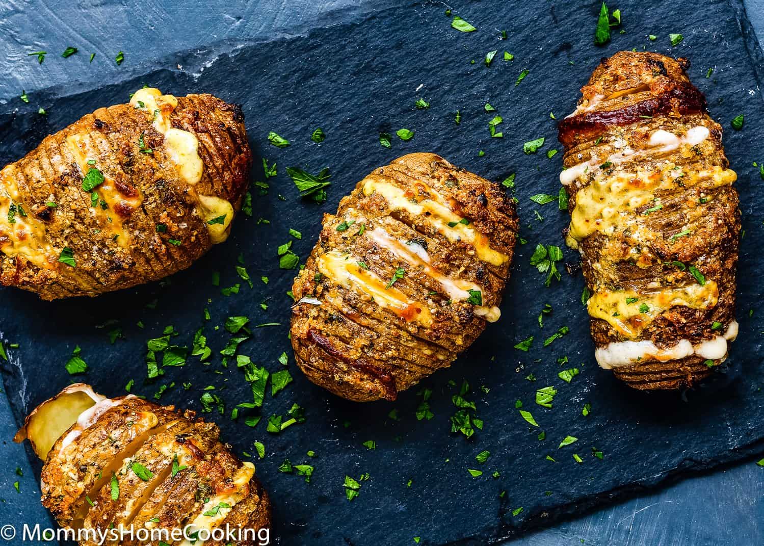 Cheesy Hasselback Potatoes with fresh parsley over a dark surface. 