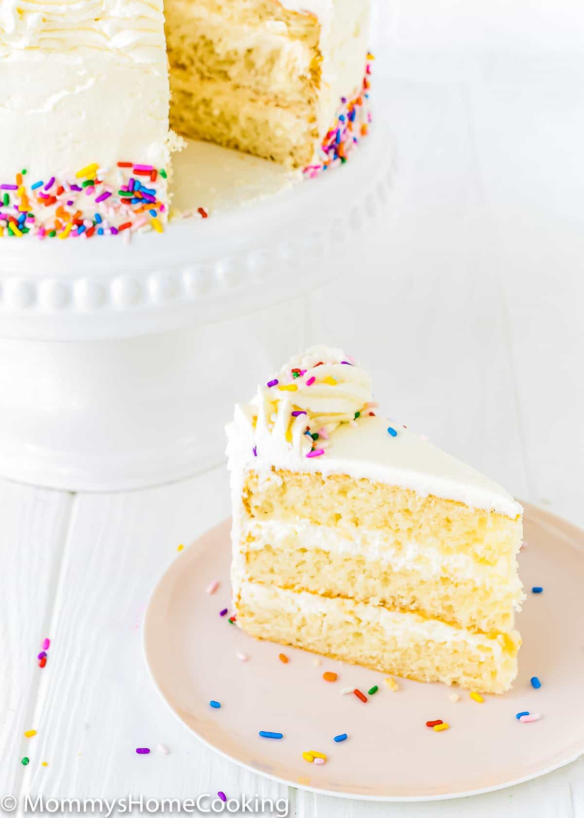 eggless vanilla cake on a cake stand next to plate with a slice of cake