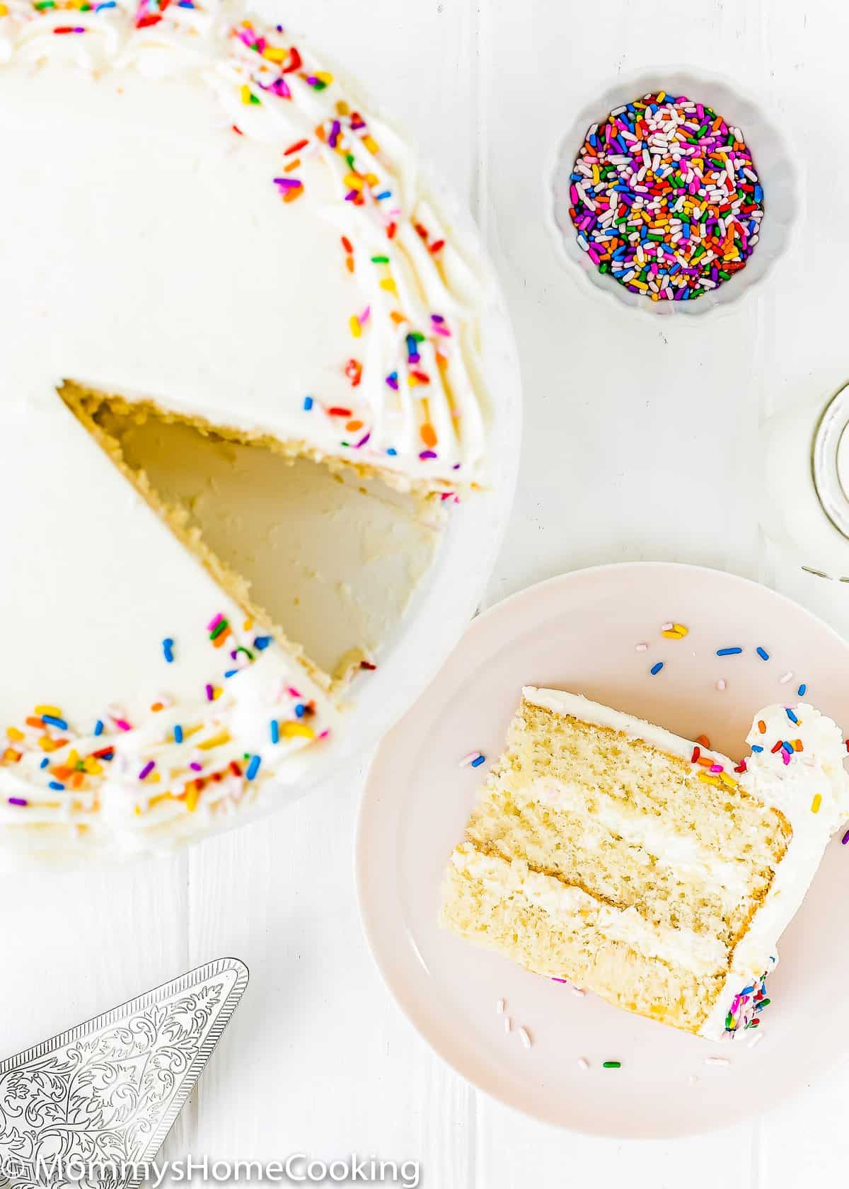 eggless vanilla cake slice on a plate with cake serving on the side.