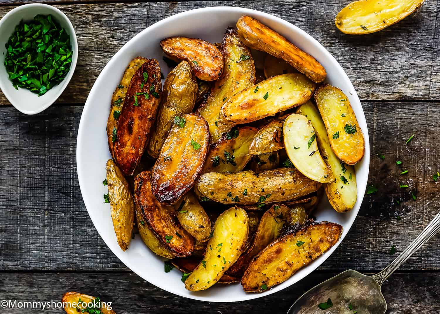 A bowl of easy garlic lemon roasted fingerling potatoes garnished with fresh herbs, resting on a rustic wooden surface.