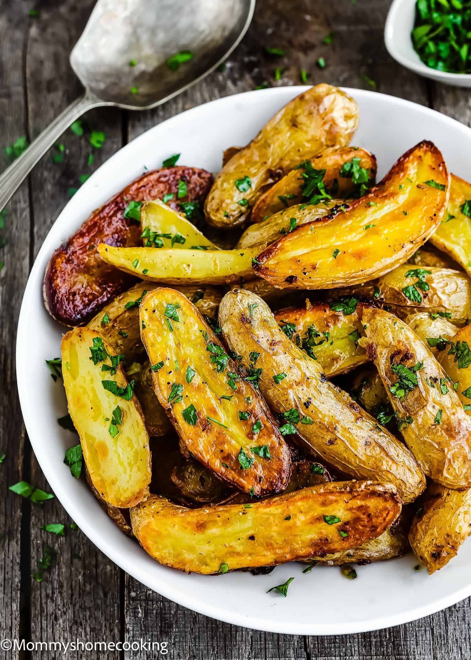 A bowl of easy garlic lemon roasted fingerling potatoes, garnished with chopped parsley, sits invitingly on a wooden table.