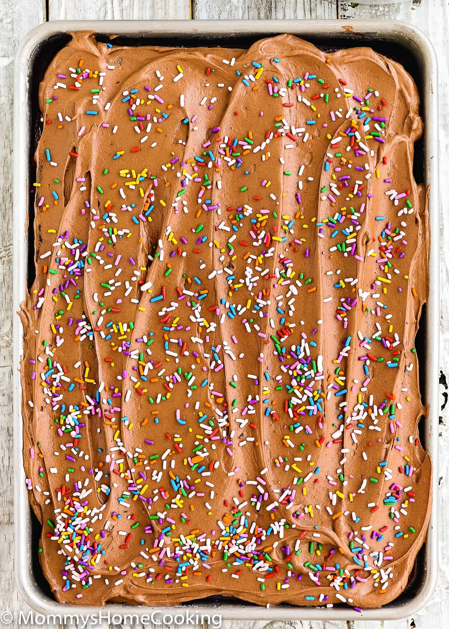 A pan of eggless chocolate cake with chocolate frosting with sprinkles on top.