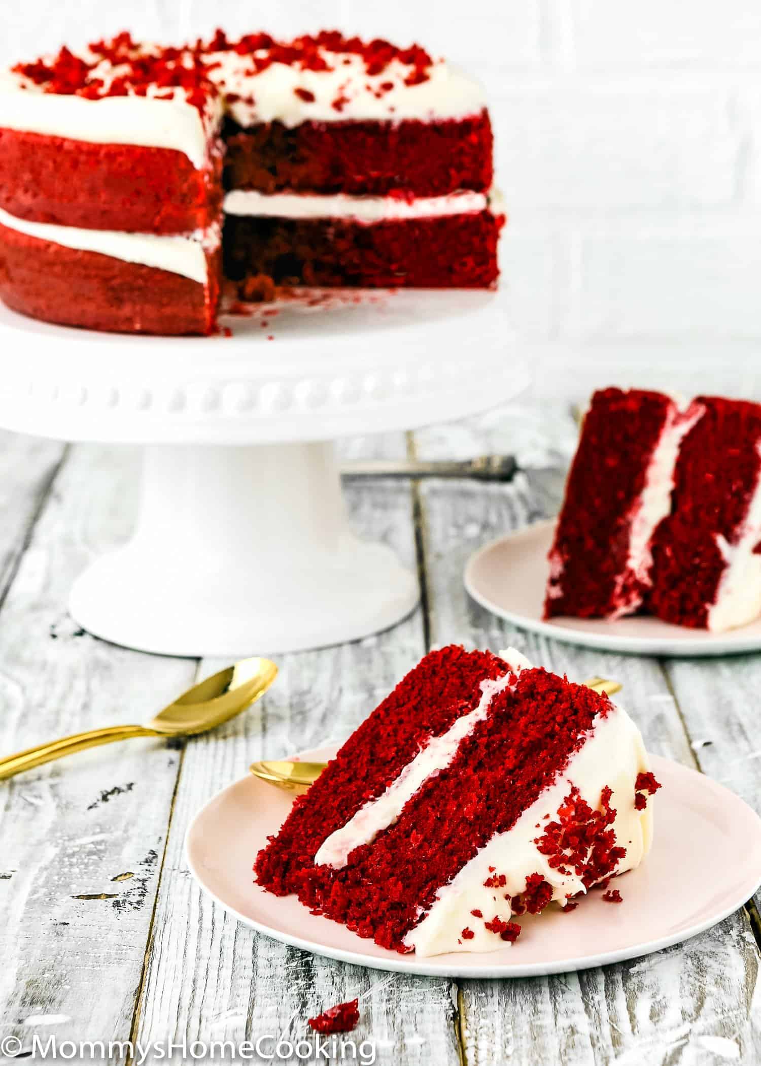 Eggless red velvet cake on a cake stand with a slice cut out, served on a plate.