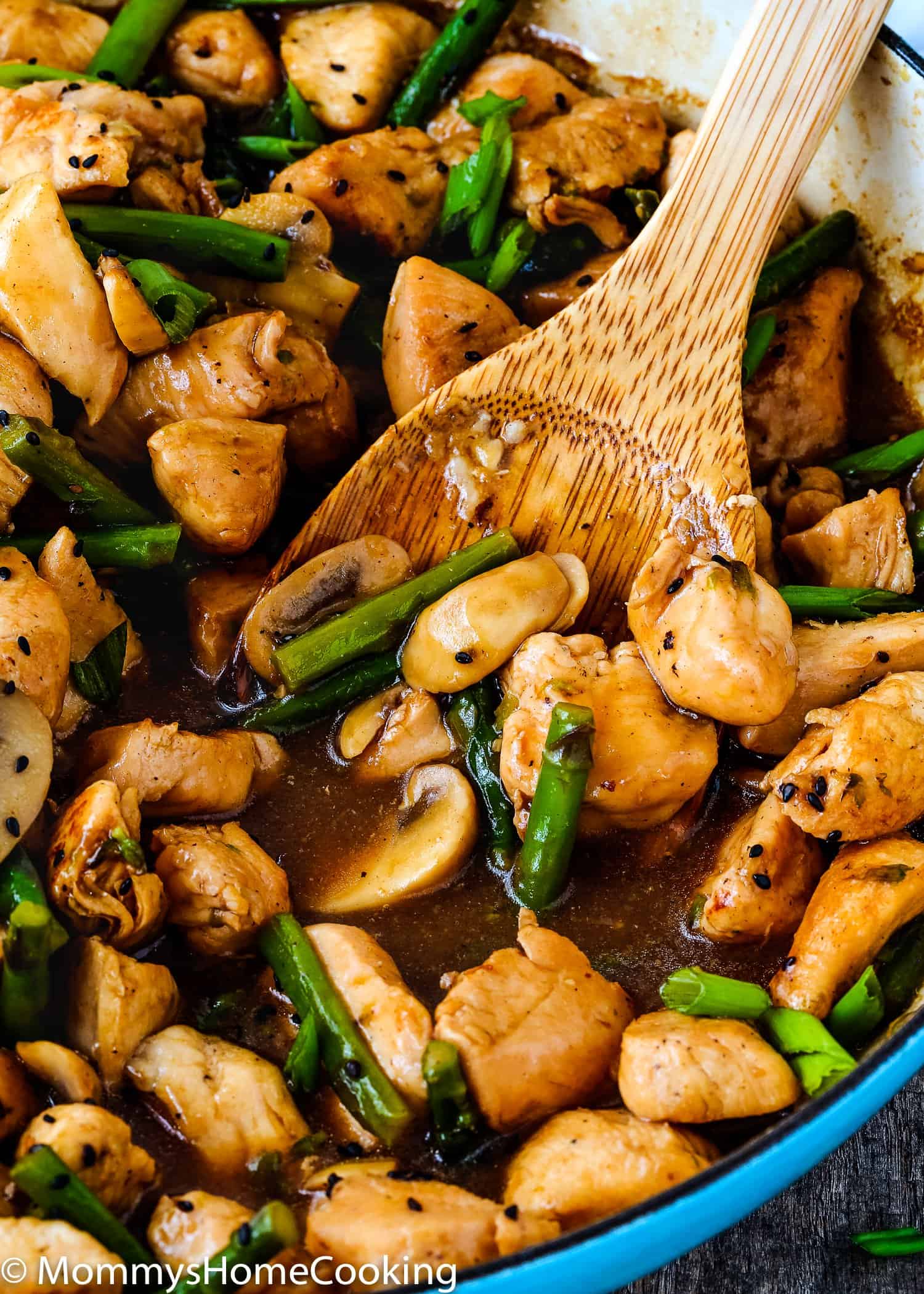 a skillet with saucy chicken, mushroom and asparagus with a wooden spoon. 
