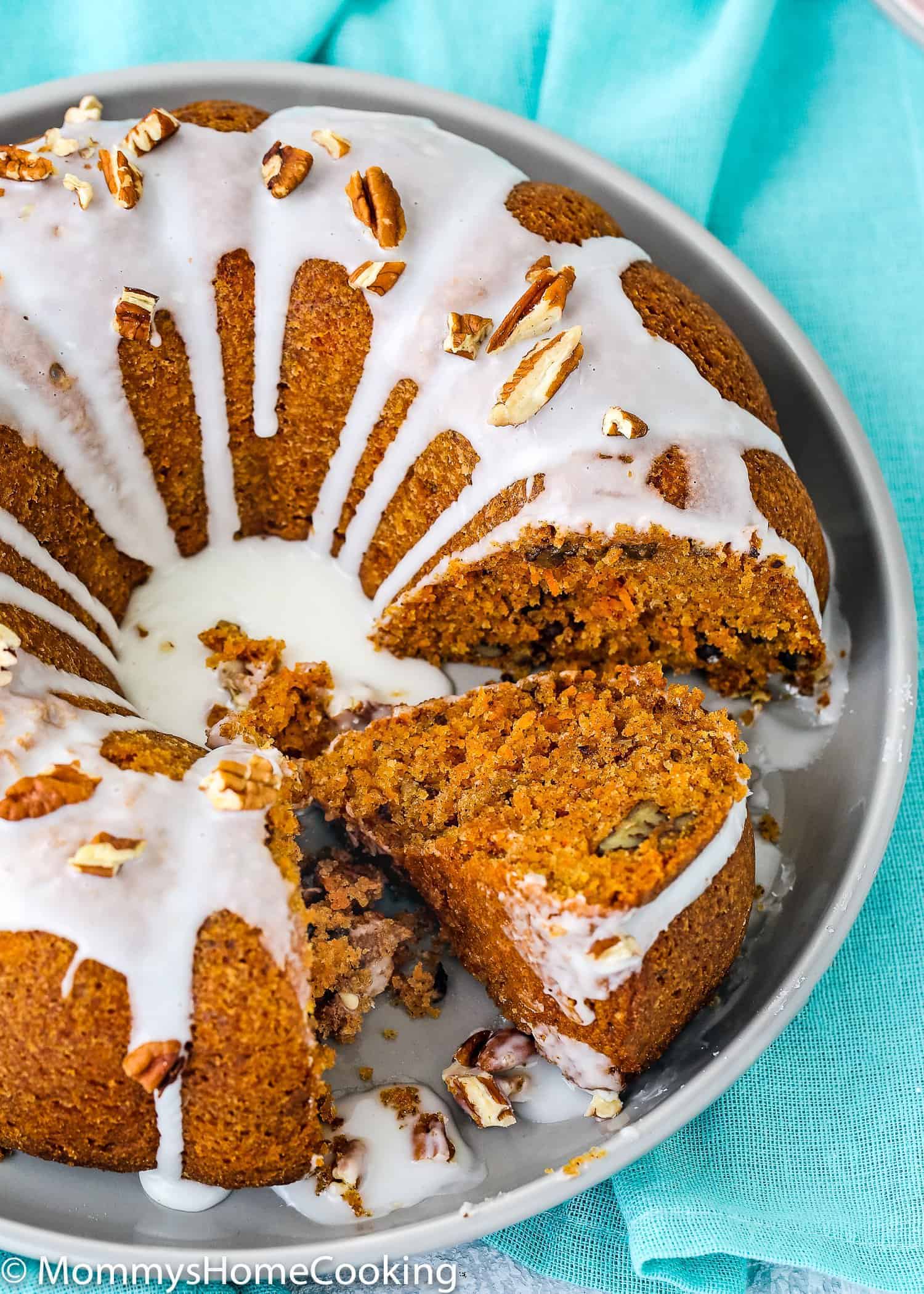 sliced eggless carrot cake on a plate with glaze and chopped pecans