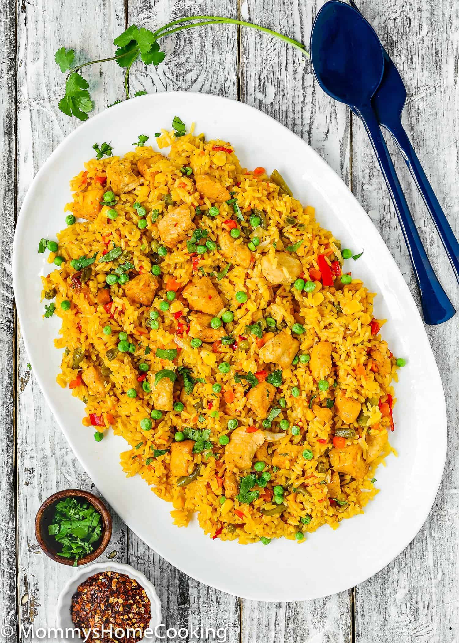 Arroz con pollo on a white serving plate with two blue serving spoons on the side.