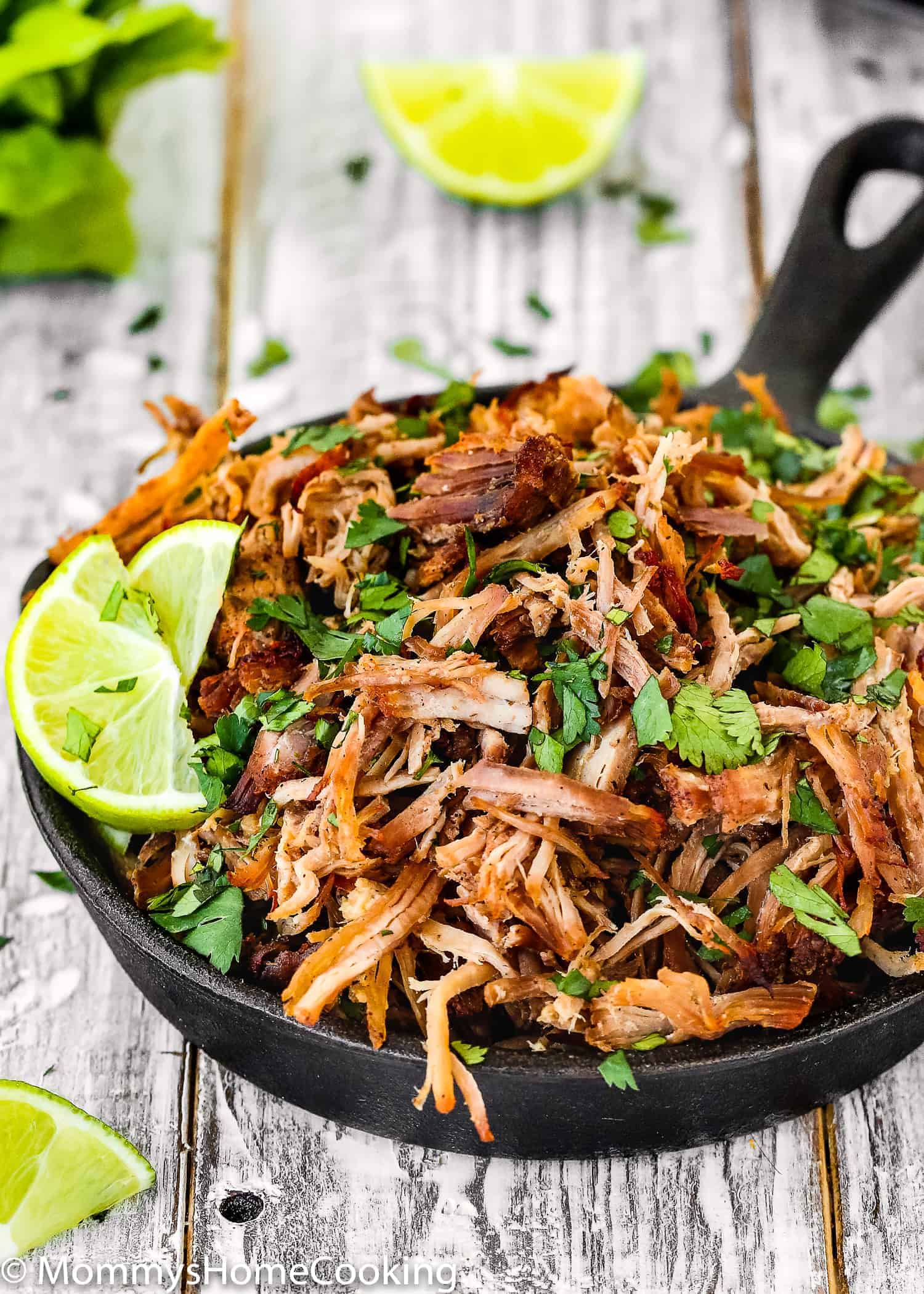 pork carnitas in a mini skillet with lemon wedges and cilantro.