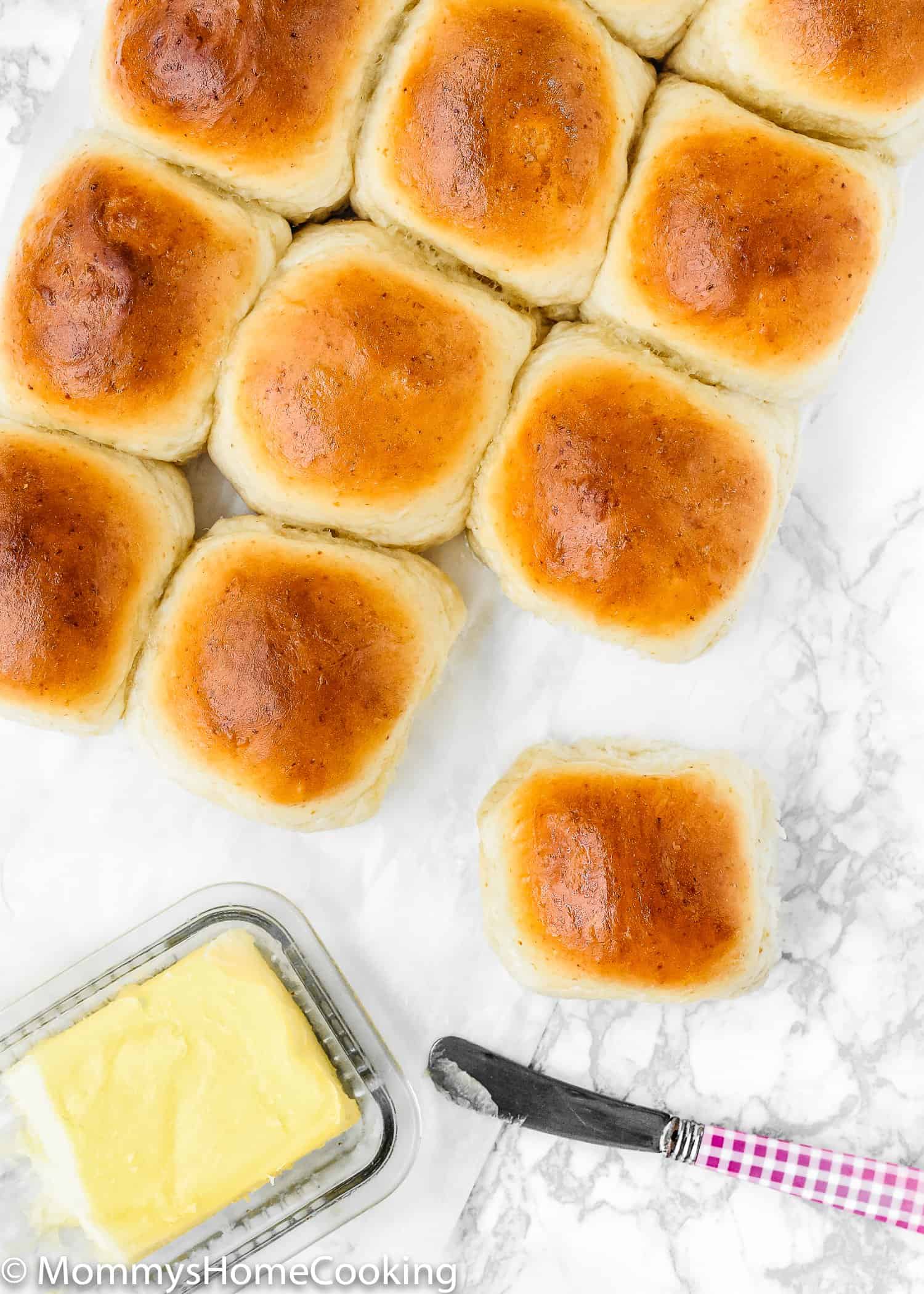 Overhead view of eggless dinner rolls beside some butter and a butter knife.