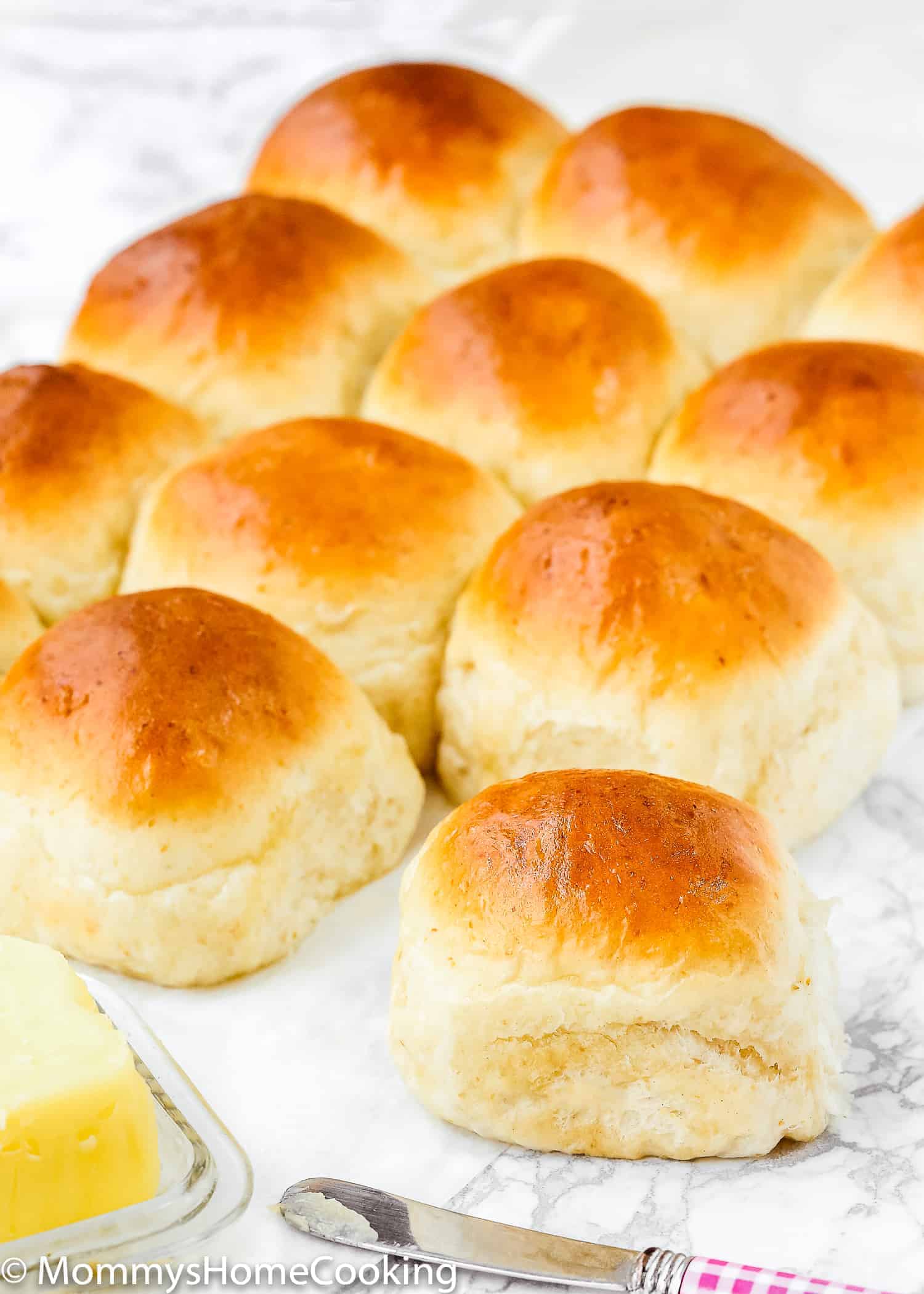 Soft No Knead Eggless Dinner Rolls with a golden crust beside butter.