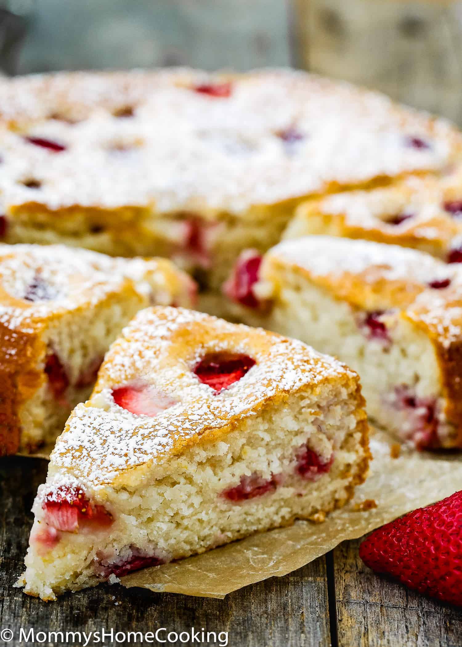 Easy Eggless Strawberry Cake sprinkled with confectioners' sugar over a parchment paper 