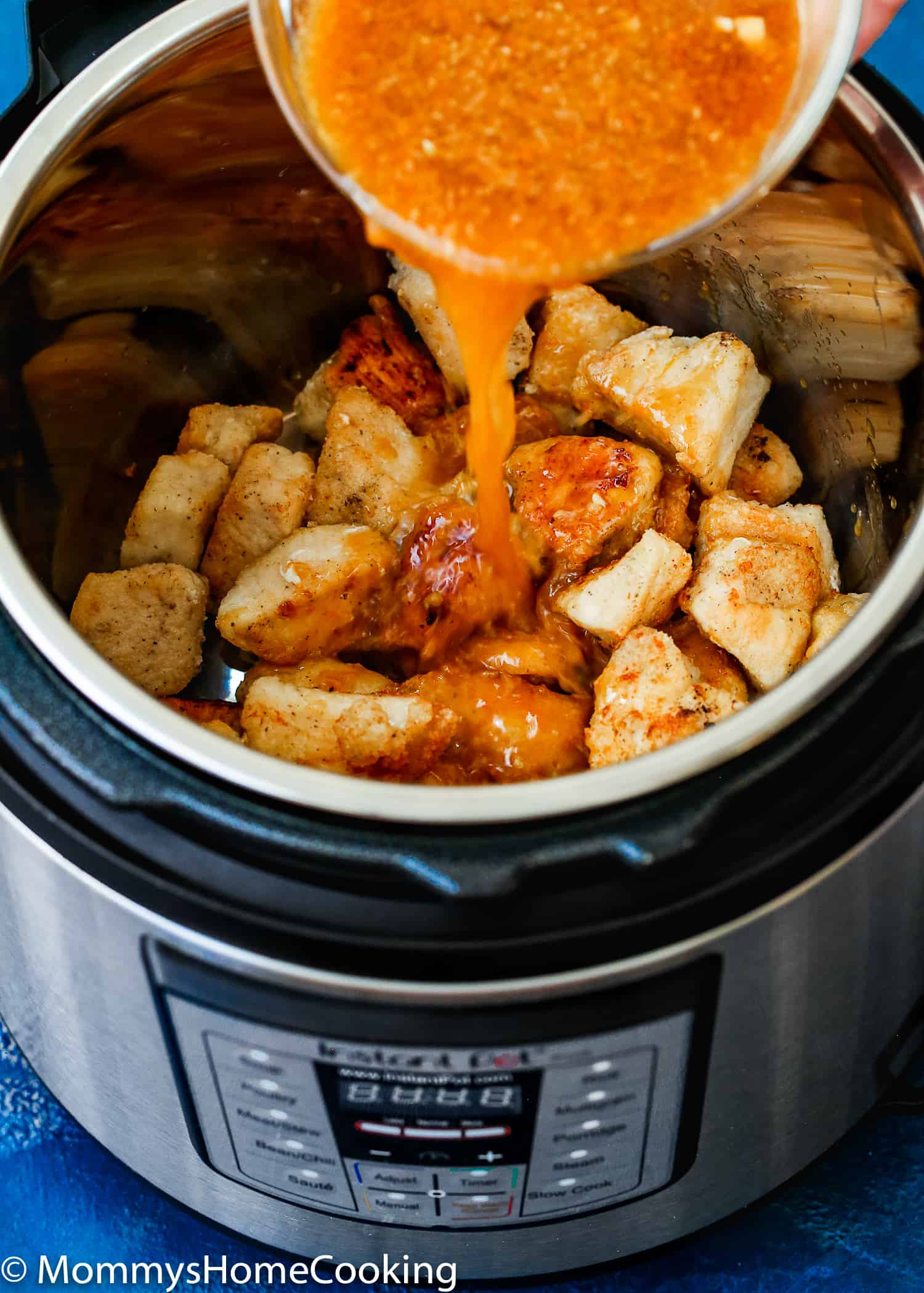 orange sauce being poured over chicken in a pressure cooker pot