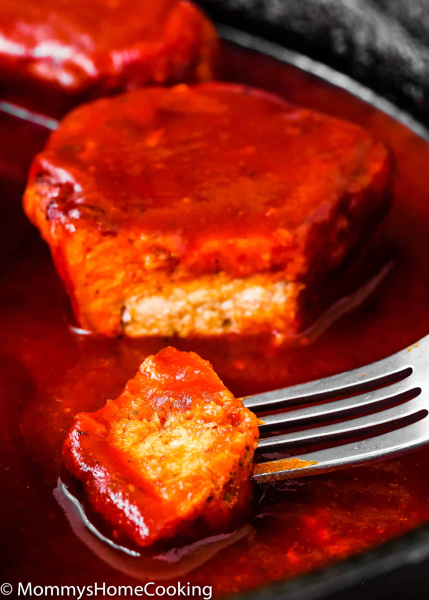 a fork holding a piece of pork in adobo sauce. 