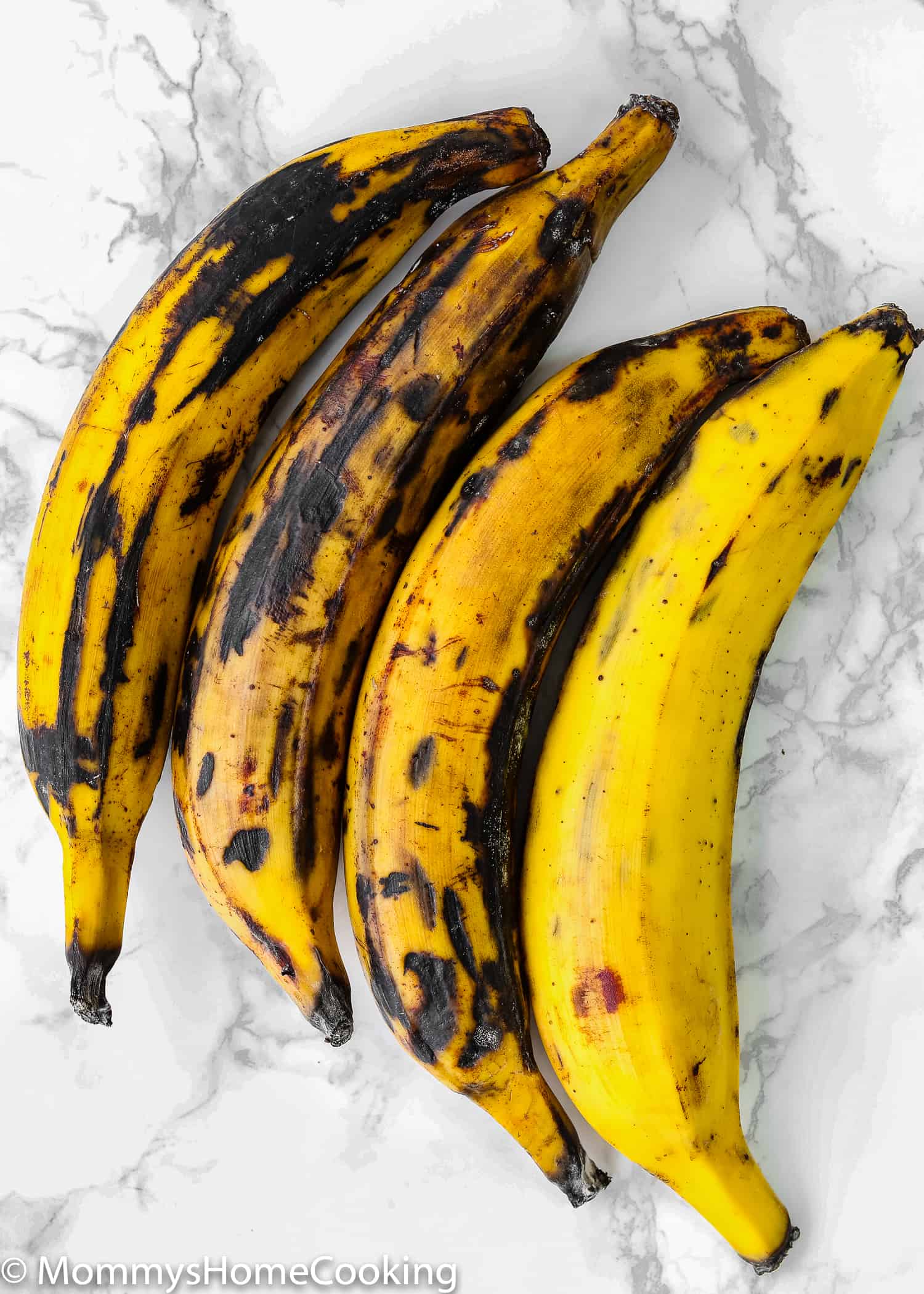 whole 4 ripe plantains over a marble surface.