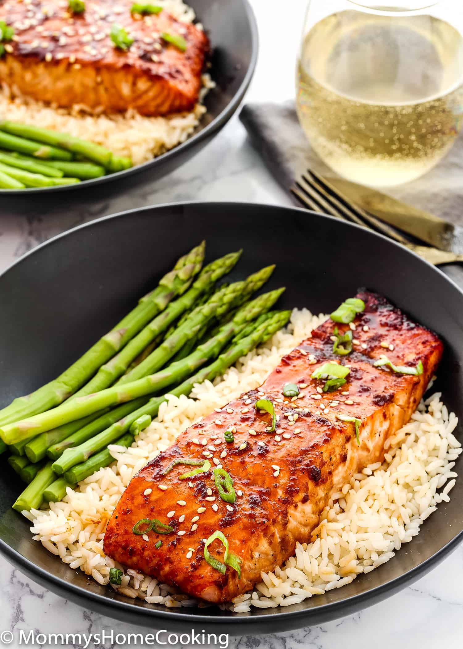 Teriyaki Salmon in a plate with white rice and asparagus and a glass of wine in the background. 