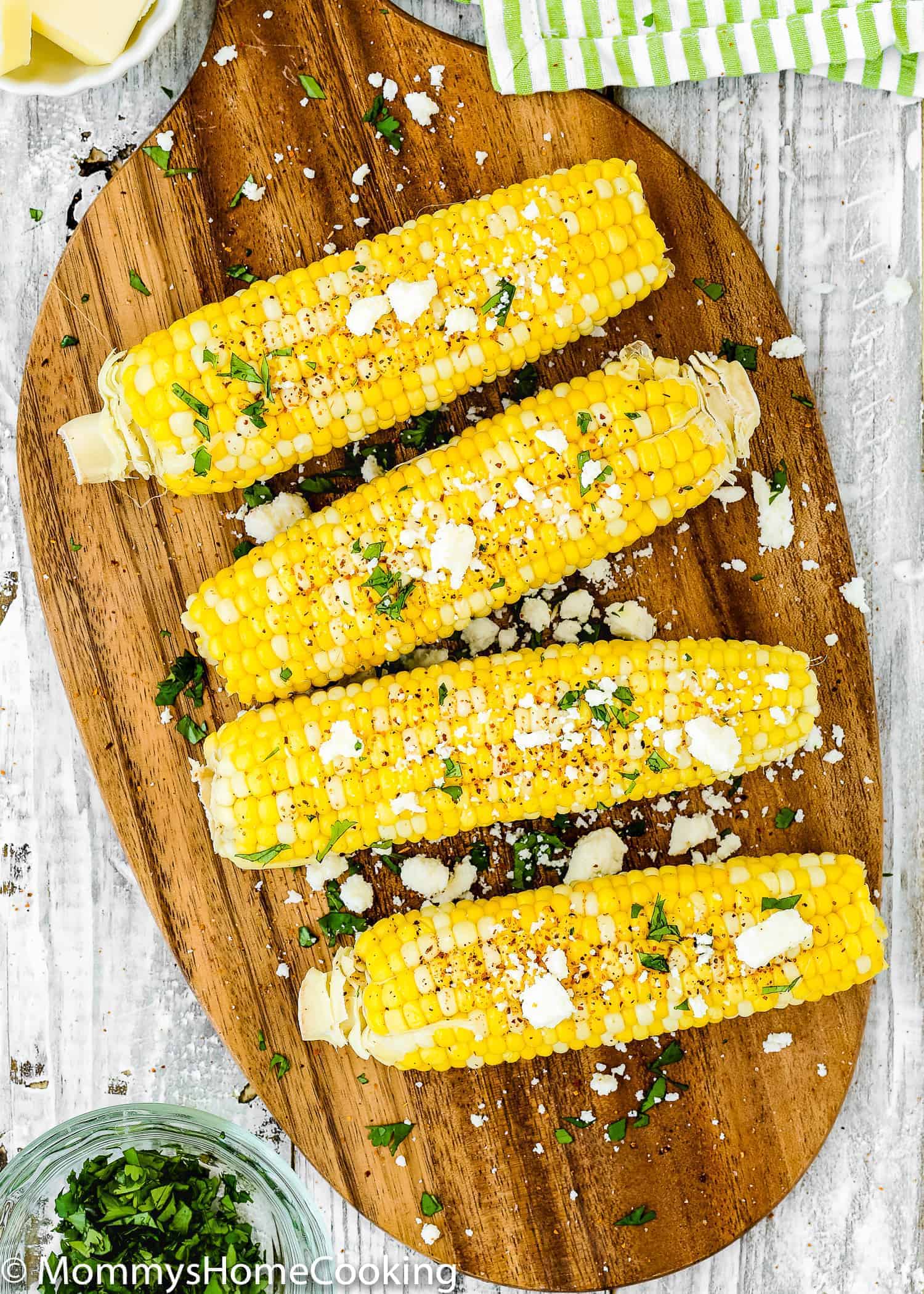 overhead view of fresh corns on the cob over a wooden tray with crumbled queso fresco, butter and tanjin. 